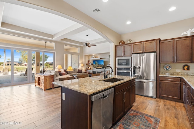 kitchen with a kitchen island with sink, sink, light stone counters, and appliances with stainless steel finishes