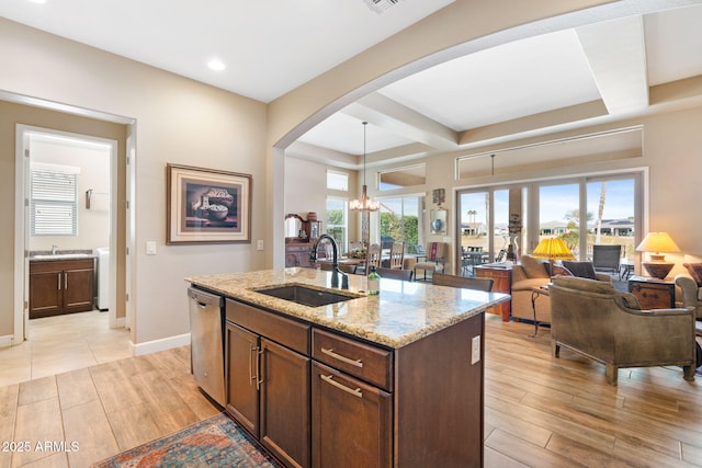 kitchen featuring sink, hanging light fixtures, a kitchen island with sink, stainless steel dishwasher, and light stone counters