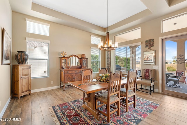 dining area with a notable chandelier, light wood-type flooring, and a tray ceiling