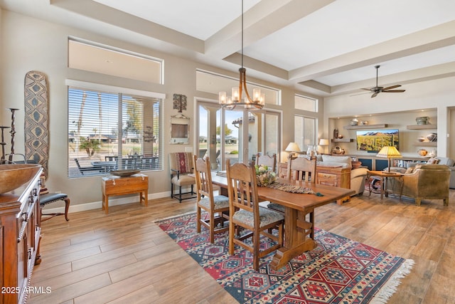 dining area with light hardwood / wood-style flooring, a raised ceiling, beam ceiling, ceiling fan with notable chandelier, and a high ceiling