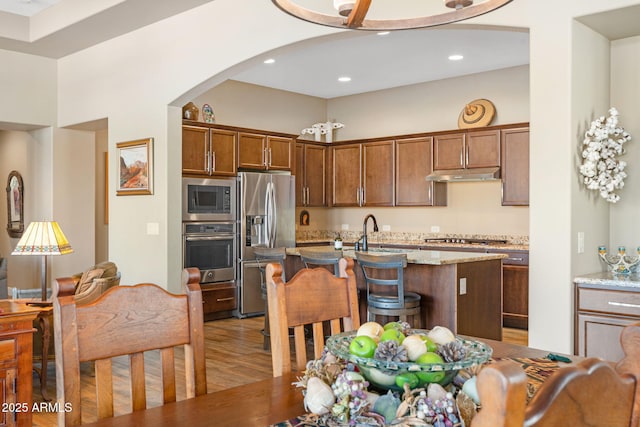 kitchen featuring sink, appliances with stainless steel finishes, an island with sink, hardwood / wood-style flooring, and light stone countertops