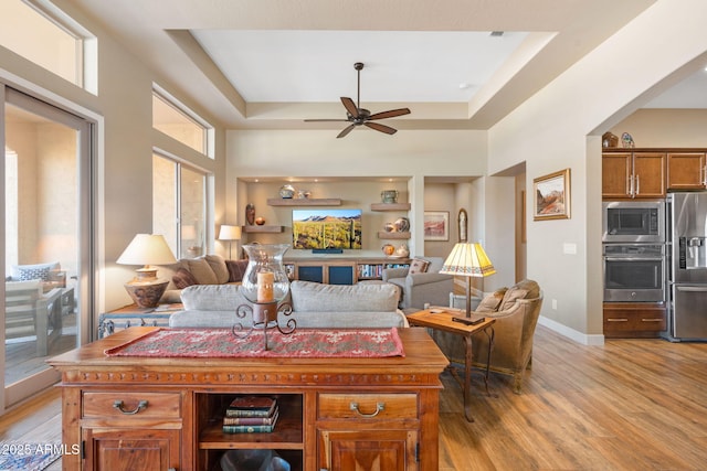 living room with a raised ceiling, ceiling fan, and light hardwood / wood-style flooring