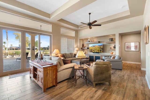 living room with hardwood / wood-style flooring, a tray ceiling, built in shelves, and french doors