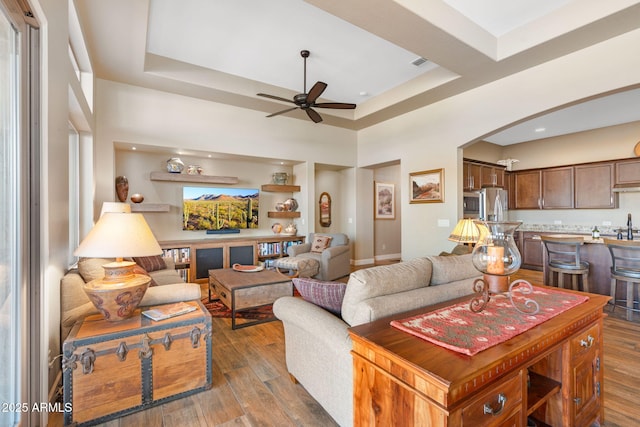 living room with a towering ceiling, dark wood-type flooring, ceiling fan, and a tray ceiling