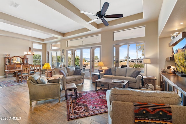 living room featuring a towering ceiling, a raised ceiling, ceiling fan with notable chandelier, and light hardwood / wood-style flooring