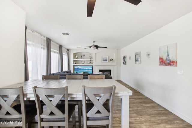 dining area featuring ceiling fan, built in shelves, dark hardwood / wood-style flooring, and a fireplace