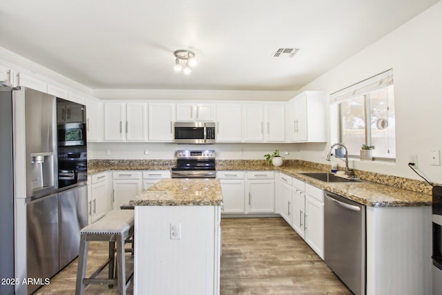 kitchen with a kitchen breakfast bar, sink, white cabinets, a kitchen island, and stainless steel appliances