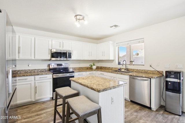 kitchen with white cabinets, a kitchen bar, stainless steel appliances, sink, and light stone counters