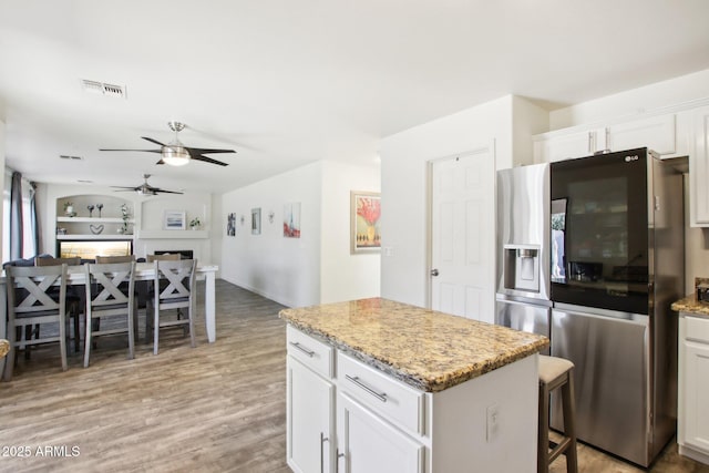 kitchen with stainless steel fridge with ice dispenser, white cabinets, a kitchen island, built in features, and light stone counters