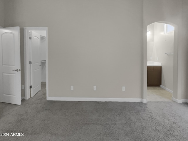 unfurnished bedroom with a walk in closet, light colored carpet, ensuite bath, and a closet