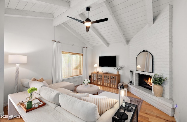 living room with ceiling fan, light hardwood / wood-style floors, a brick fireplace, and lofted ceiling with beams