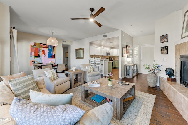 living room with ceiling fan, dark wood-type flooring, and a tile fireplace