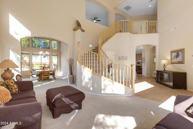 carpeted living room featuring ceiling fan with notable chandelier and a high ceiling