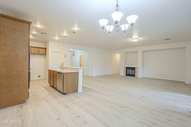 kitchen featuring visible vents, brown cabinets, a fireplace, light wood-style floors, and stainless steel dishwasher