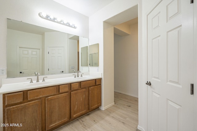 full bath with a sink, baseboards, wood finished floors, and double vanity