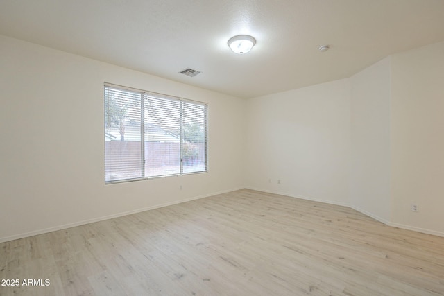 spare room with light wood-type flooring, visible vents, and baseboards