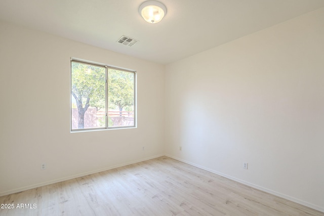 spare room featuring light wood finished floors, visible vents, and baseboards