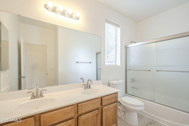 bathroom featuring double vanity, shower / bath combination with glass door, toilet, and a sink