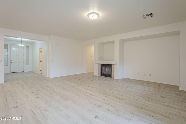 unfurnished living room featuring visible vents, light wood finished floors, and a tile fireplace