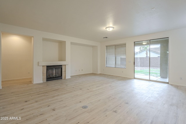 unfurnished living room featuring visible vents, baseboards, light wood-style floors, and a tile fireplace