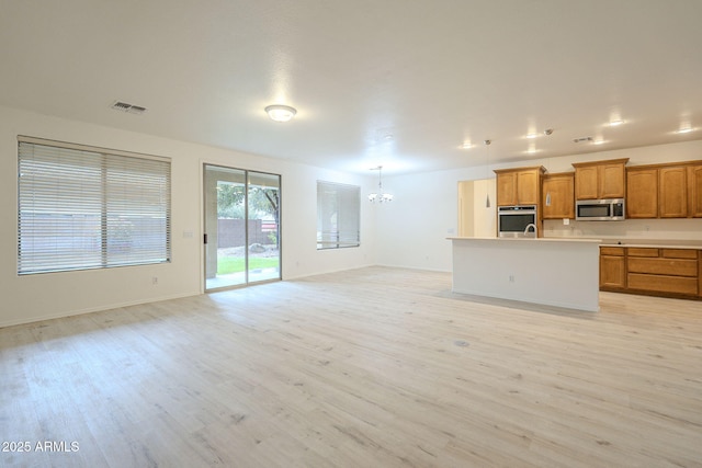 kitchen with brown cabinetry, open floor plan, appliances with stainless steel finishes, and light wood-style floors