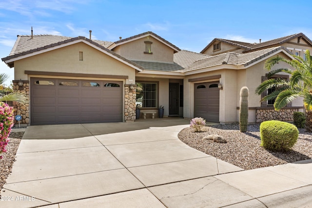 view of front of property featuring stucco siding, stone siding, a tiled roof, driveway, and a garage