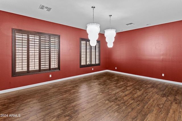 spare room with visible vents, an inviting chandelier, and wood finished floors