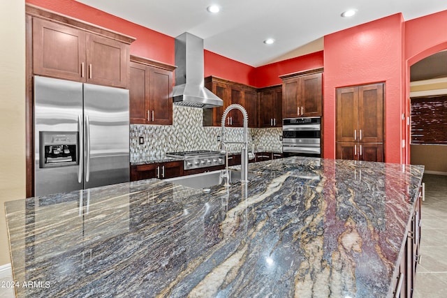 kitchen with appliances with stainless steel finishes, wall chimney range hood, dark stone countertops, backsplash, and vaulted ceiling