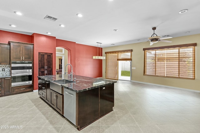 kitchen with visible vents, a kitchen island with sink, stainless steel appliances, a ceiling fan, and arched walkways