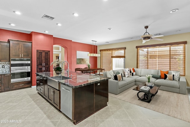 kitchen featuring appliances with stainless steel finishes, dark stone countertops, visible vents, arched walkways, and ceiling fan