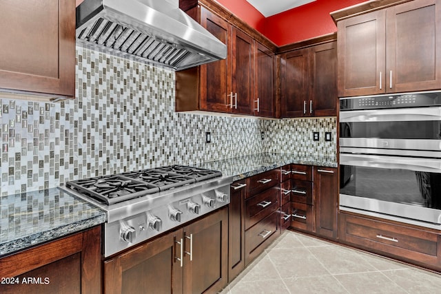 kitchen featuring wall chimney exhaust hood, backsplash, dark stone counters, and appliances with stainless steel finishes