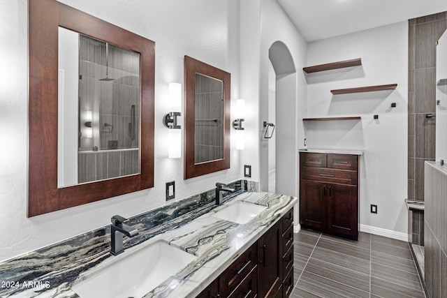 full bathroom featuring double vanity, a tile shower, baseboards, and a sink