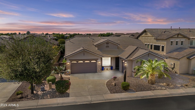 view of front of home featuring stone siding, a tiled roof, a garage, stucco siding, and driveway