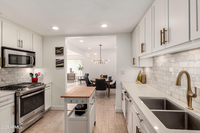 kitchen featuring a sink, white cabinetry, appliances with stainless steel finishes, light wood finished floors, and wooden counters