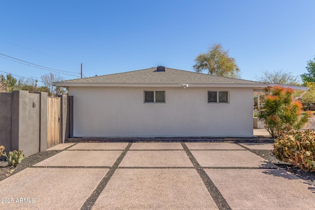 view of home's exterior featuring stucco siding, roof with shingles, and a gate
