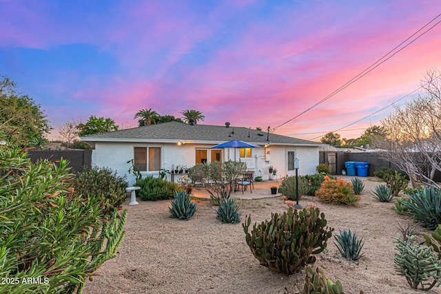 rear view of house with stucco siding, roof with shingles, a fenced backyard, and a patio area