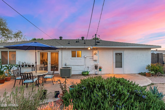 back of property at dusk featuring stucco siding, a patio, fence, cooling unit, and french doors
