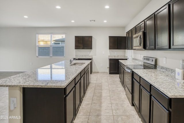 kitchen featuring dark brown cabinetry, stainless steel appliances, light stone counters, light tile patterned floors, and a center island with sink