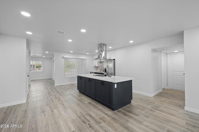 kitchen featuring sink, stainless steel refrigerator with ice dispenser, light hardwood / wood-style flooring, a large island, and island range hood