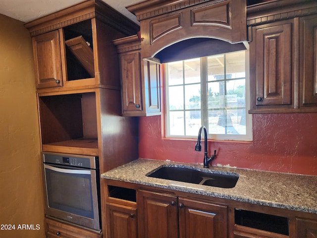 kitchen with stainless steel oven, light stone counters, and sink