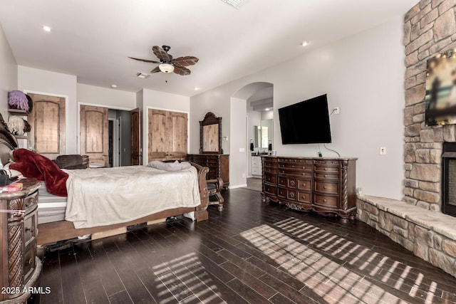 bedroom featuring dark hardwood / wood-style flooring, a stone fireplace, and ceiling fan