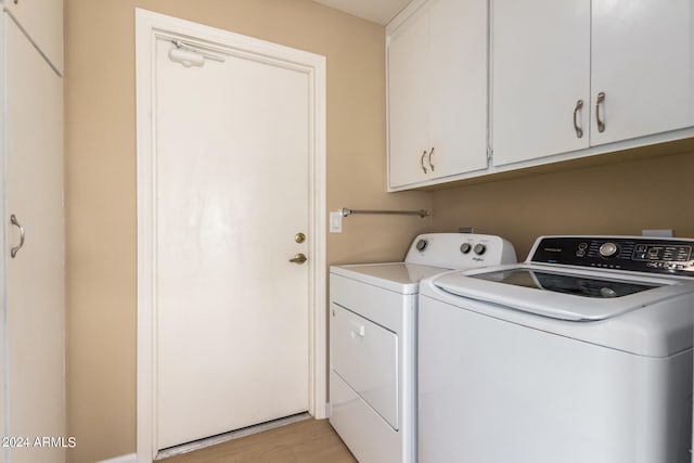 clothes washing area featuring independent washer and dryer, light wood-type flooring, and cabinets