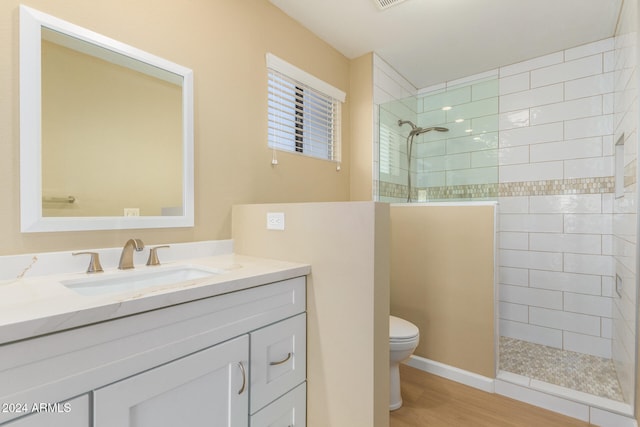 bathroom with toilet, hardwood / wood-style floors, vanity, and a tile shower