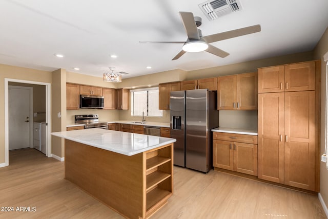 kitchen featuring ceiling fan, light wood-type flooring, stainless steel appliances, a center island, and washer and clothes dryer