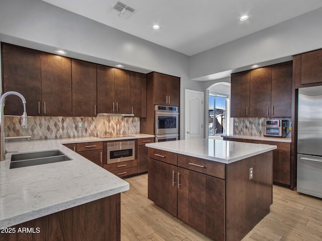 kitchen with dark brown cabinetry, sink, a kitchen island, stainless steel appliances, and light hardwood / wood-style floors