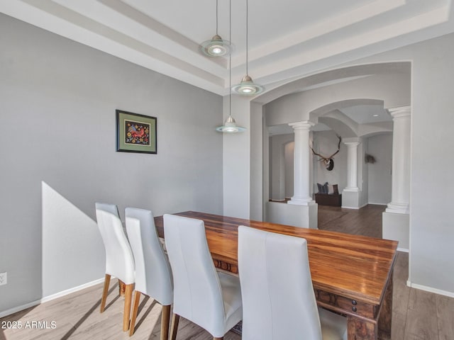 dining space with ornate columns, wood-type flooring, and a tray ceiling