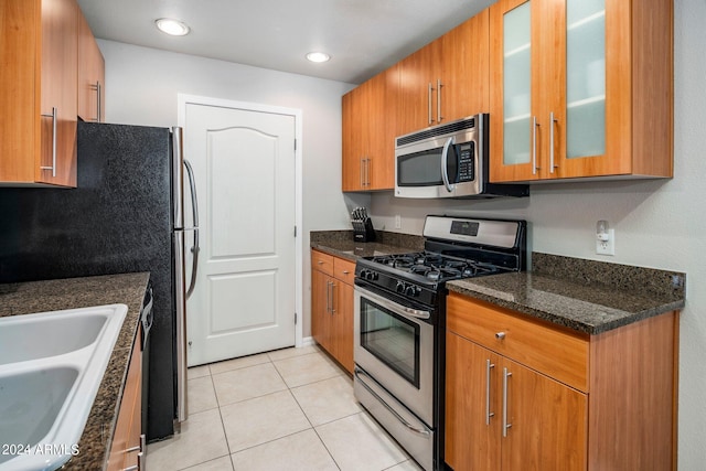 kitchen with stainless steel appliances, dark stone countertops, light tile patterned floors, and sink