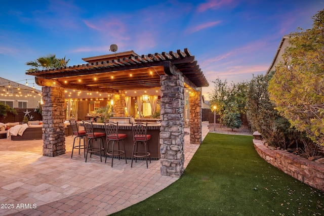 patio terrace at dusk featuring a bar, outdoor lounge area, and a lawn