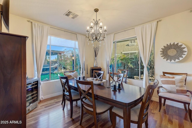 dining area with wine cooler, wood-type flooring, and a chandelier