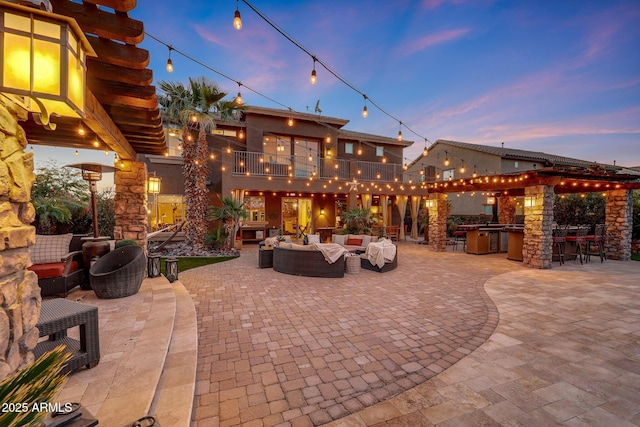 patio terrace at dusk with an outdoor kitchen, outdoor lounge area, a balcony, and exterior bar